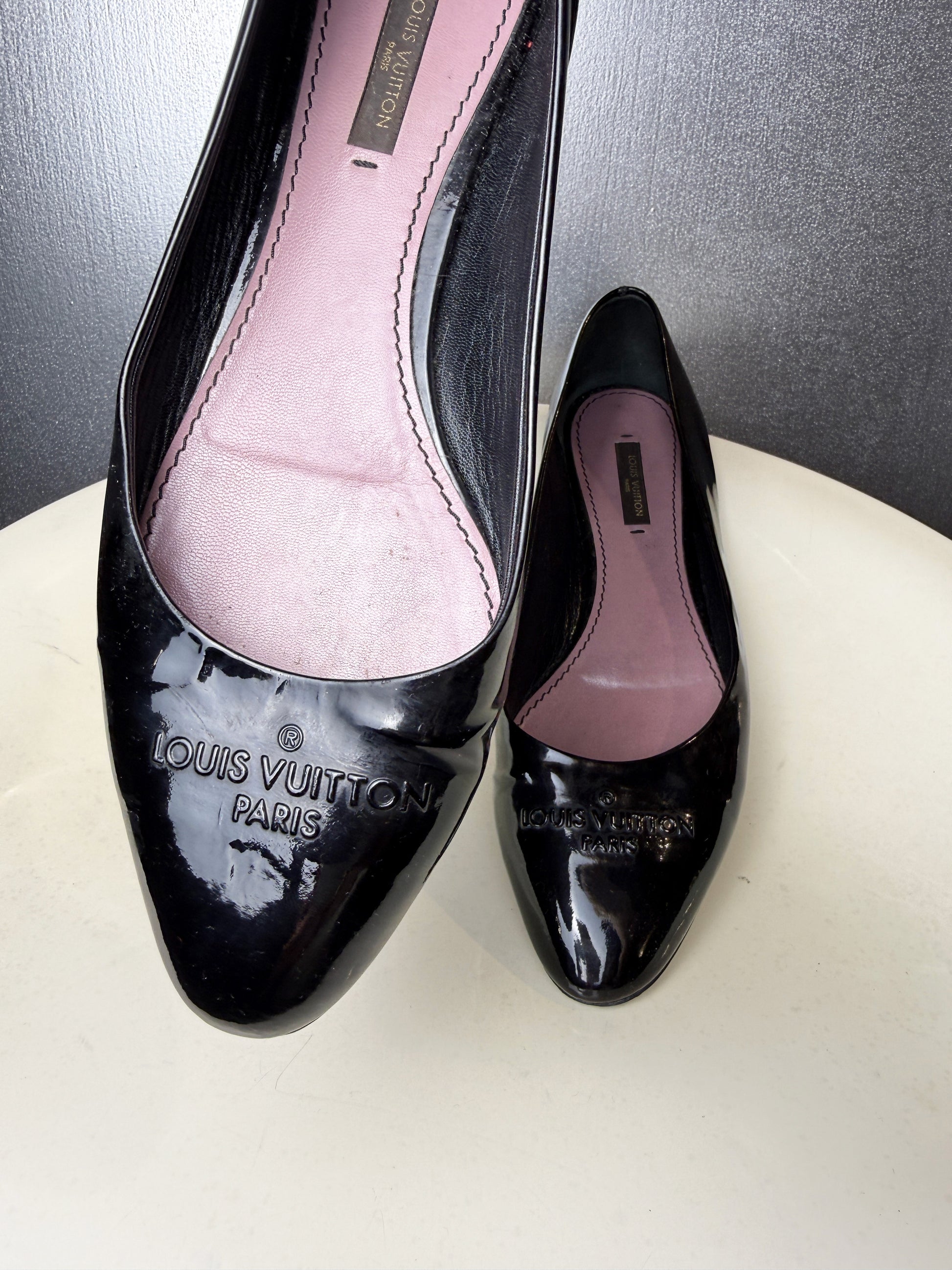 Embossed Louis Vuitton Paris logo on black patent leather ballet flat.